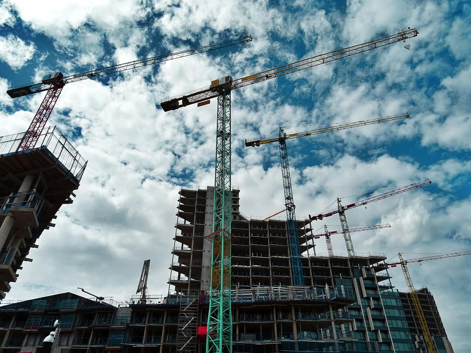 Urban construction site with numerous cranes framing rising skyscrapers against a blue sky. design build