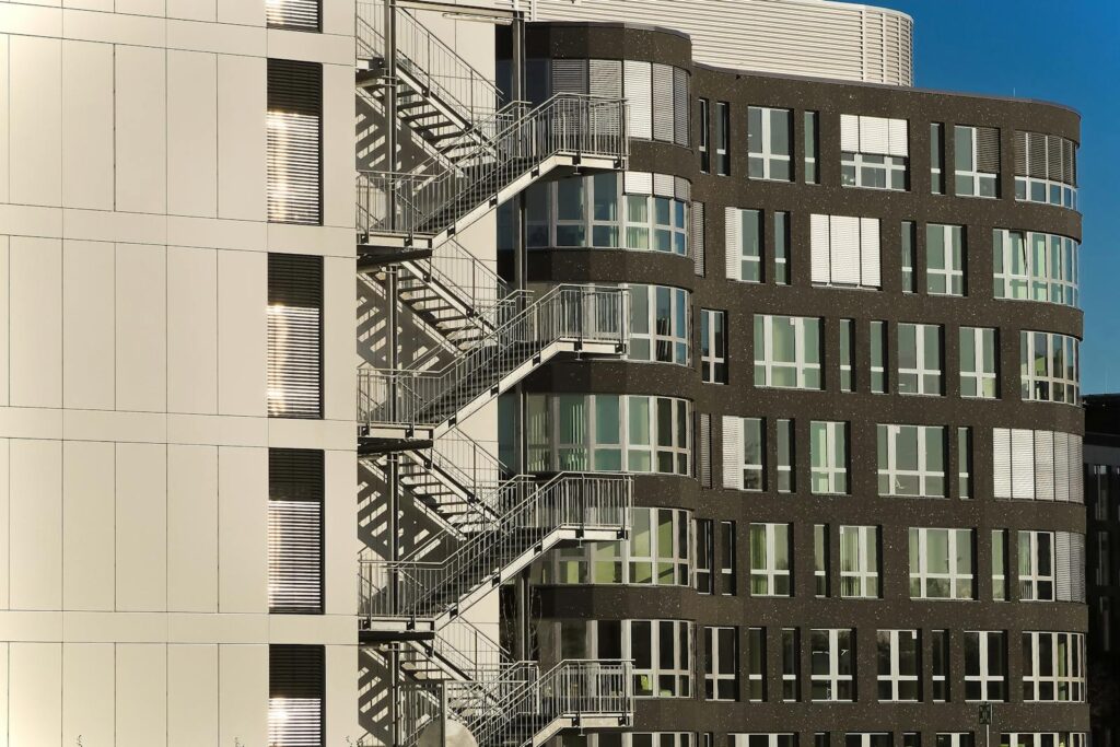 A contemporary building facade with steel staircases and glass windows under clear skies.