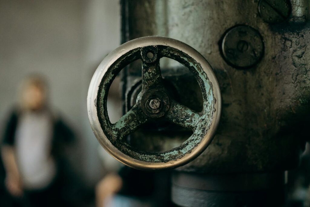 Close-up of a rustic metallic valve in an industrial setting, emphasizing texture and wear.