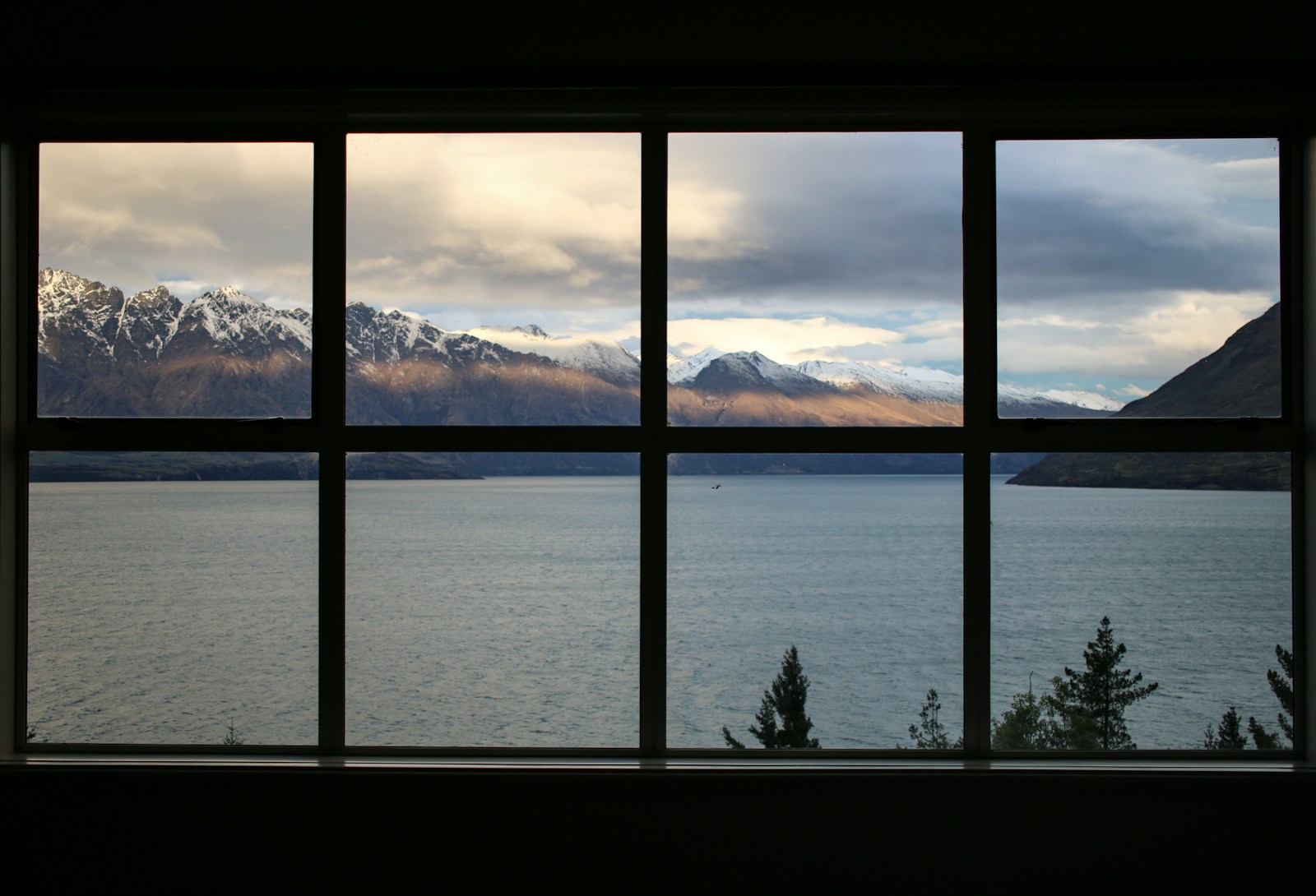 calm body of water near brown mountain under white and gray sky types of windows