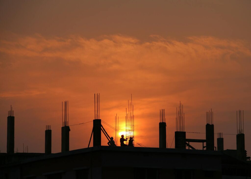 Silhouette of workers on a construction site against a vibrant sunset sky.