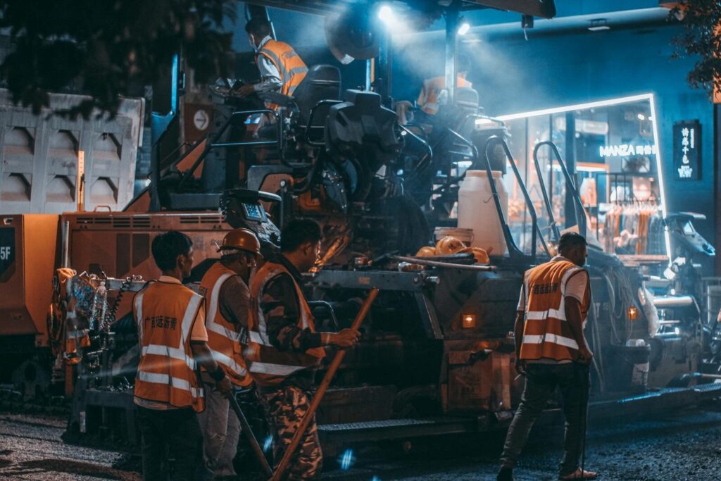 Road construction crew at work with machinery and lights during the night.