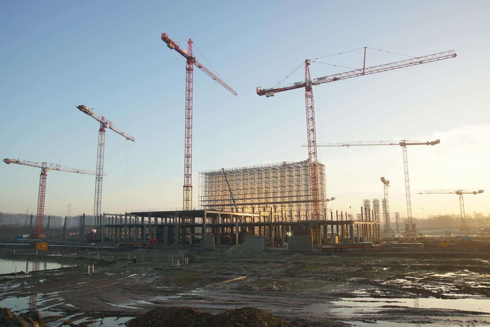 Wide view of a construction site with cranes and building framework at sunset. Industrial landscape.