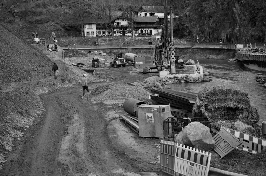 Monochrome image of construction site next to a river with heavy machinery and workers.