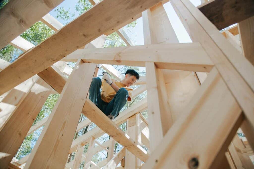 Carpenter working on the wooden structure of a house at a construction site under the sun.