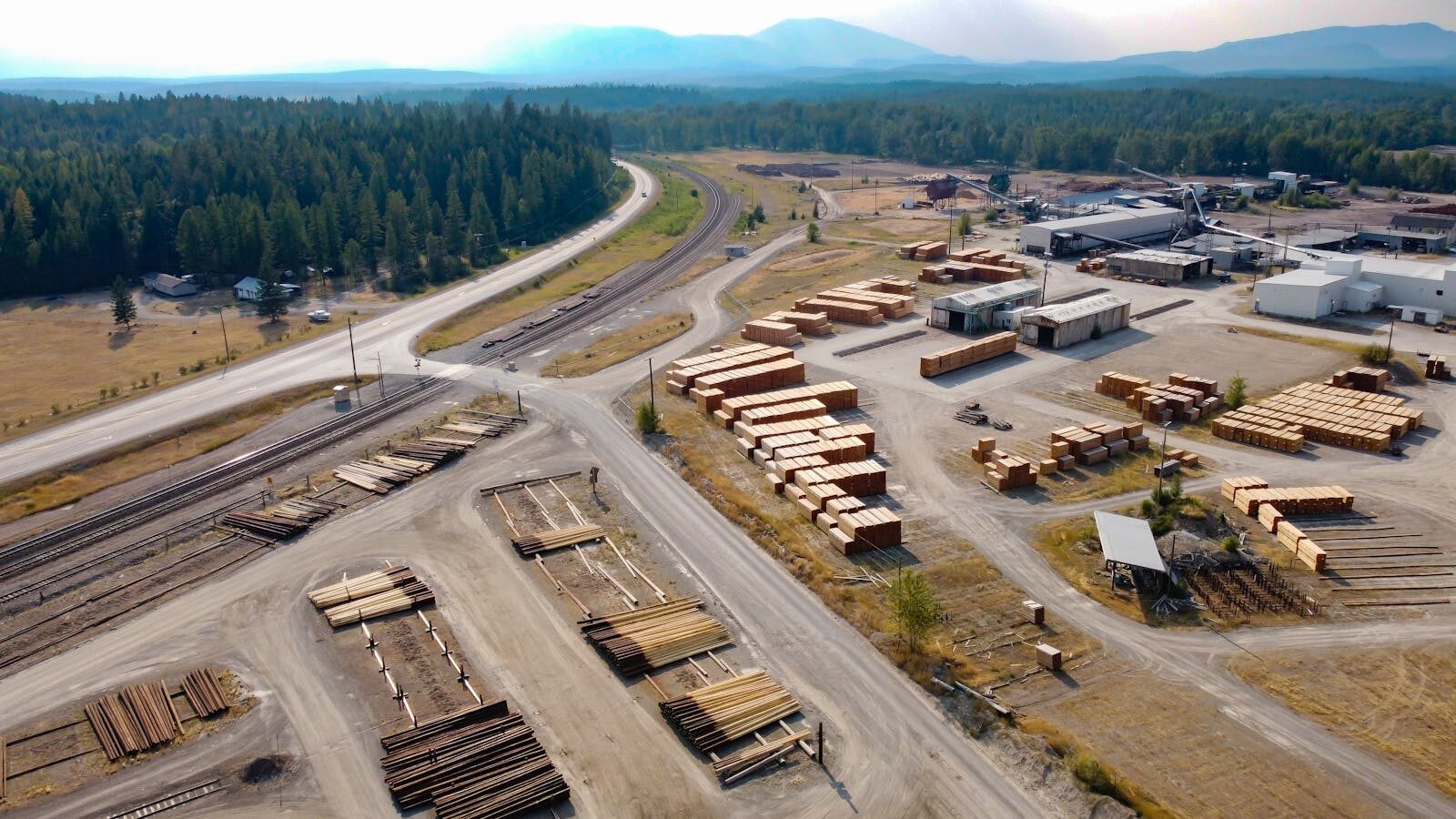 Aerial view of a large lumber yard and sawmill in rural Jaffray, BC, Canada, showcasing industrial logging activities.