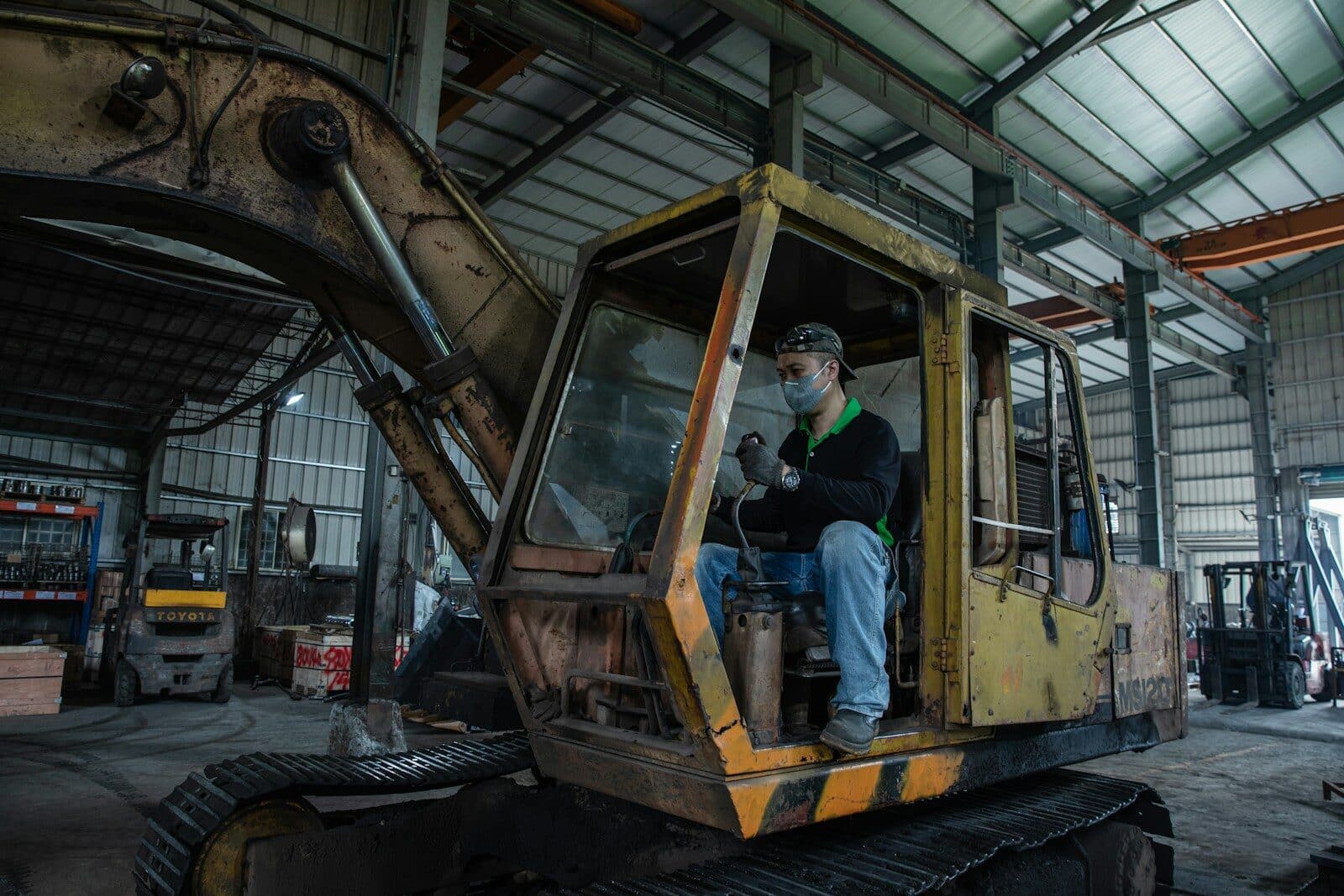 Man sits in an old excavator in a workshop.