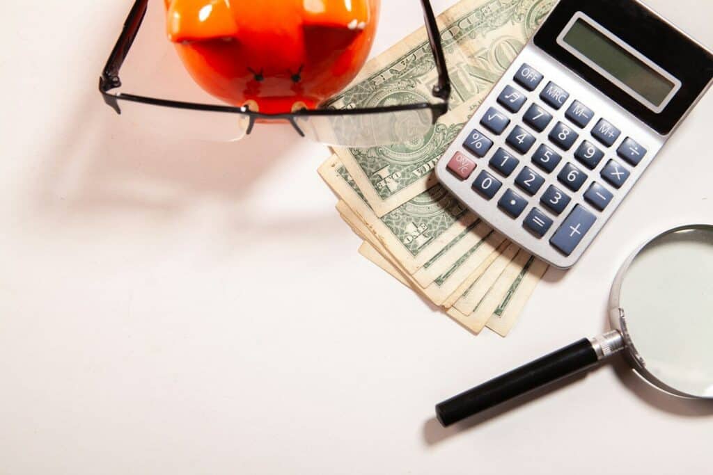 Calculator, magnifying glass, glasses, and money on white surface.
