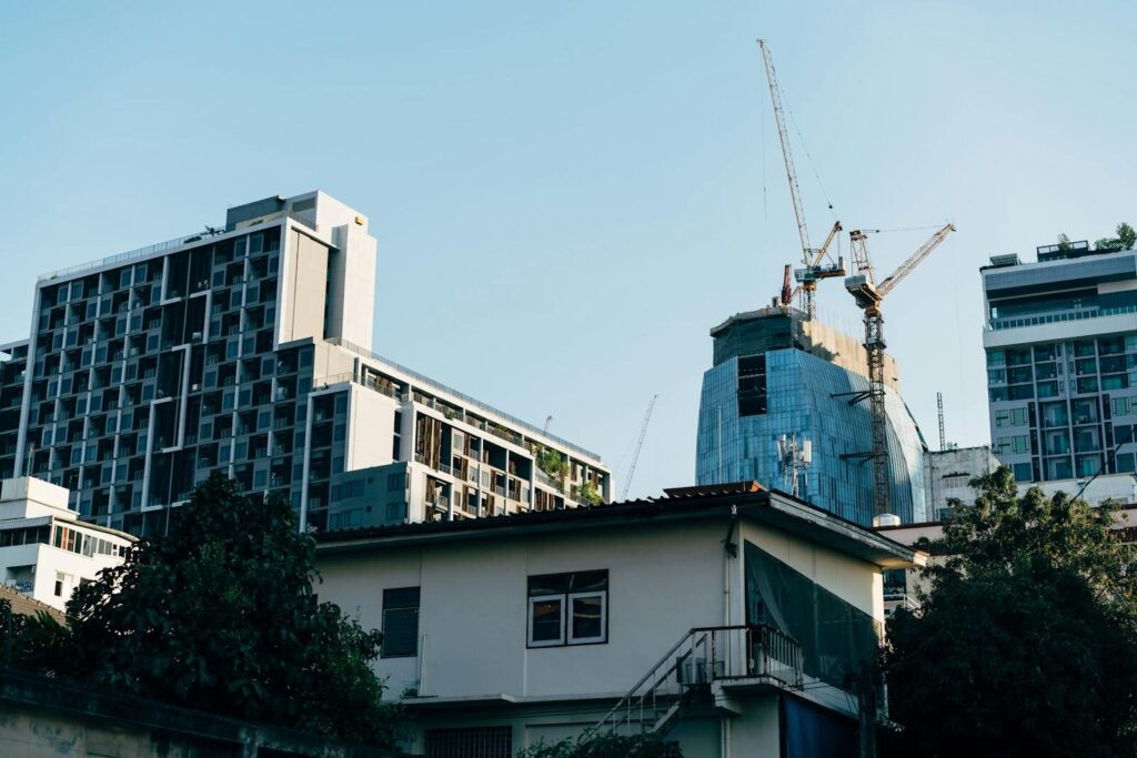 View of a city skyline with contemporary buildings and cranes under blue sky.