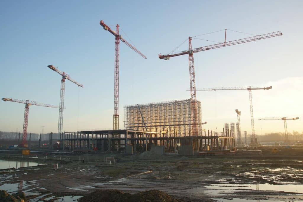 Wide view of a construction site with cranes and building framework at sunset. Industrial landscape.