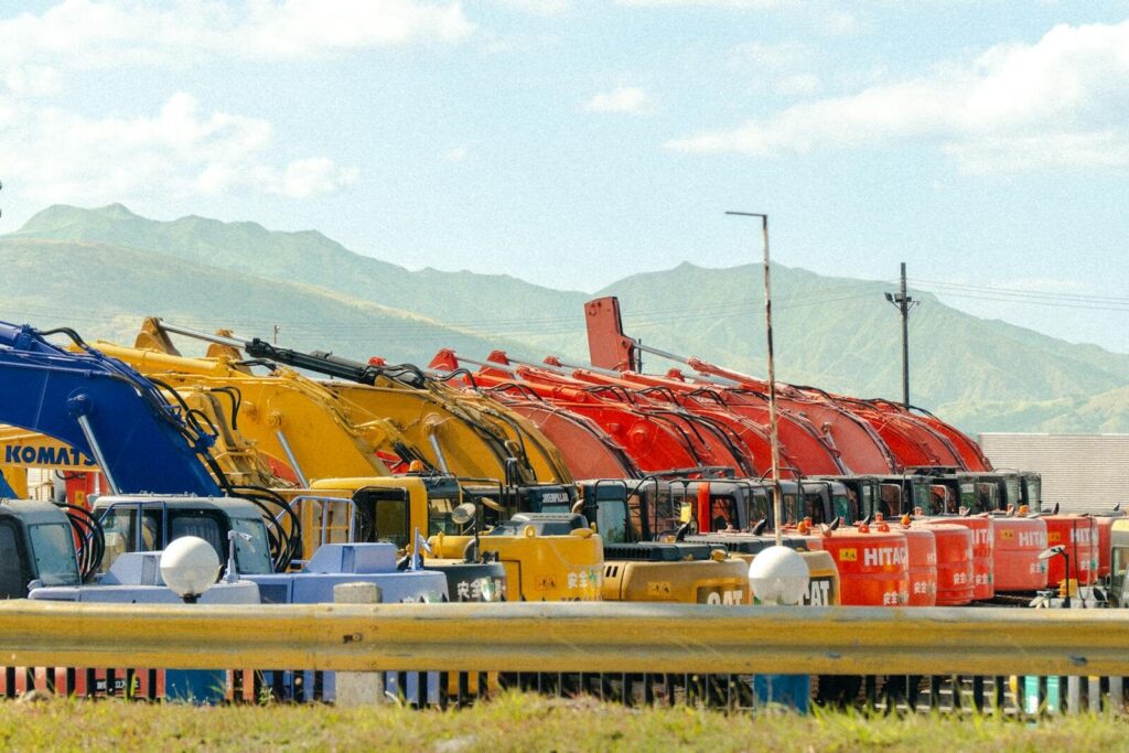 A lineup of vibrant construction vehicles against a beautiful mountain backdrop.