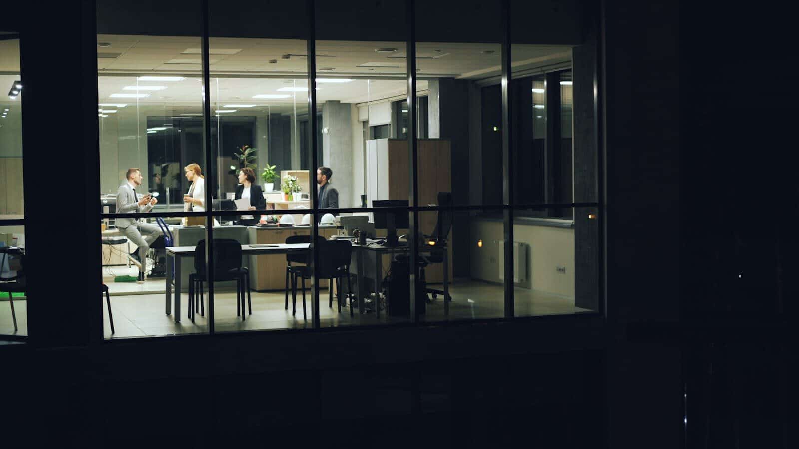 A nighttime office meeting with professionals working in a modern glass-walled office. Top 10 Most Successful Businesses to Start and How the Right Construction Partner Helps