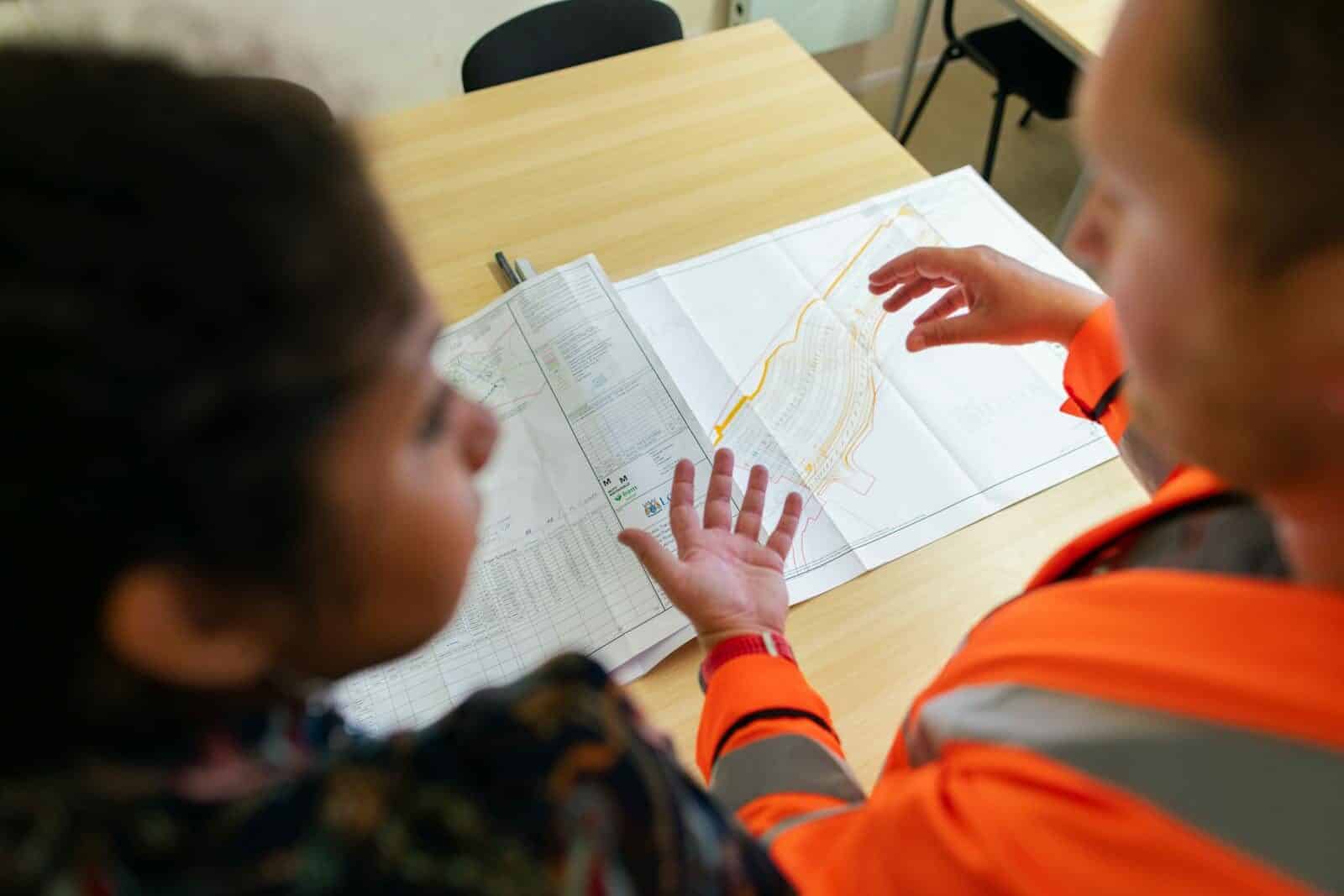 Two engineers reviewing construction blueprints on a table in an office setting. What Does a Civil Engineer Do in a Construction Project?