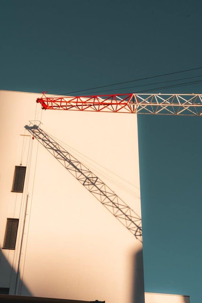 Red and white crane casts shadow on a white building.