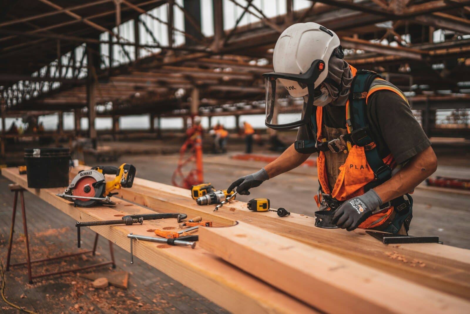 man in orange and black vest wearing white helmet holding yellow and black power tool What Is A Contractor? A Guide For Commercial Construction Clients